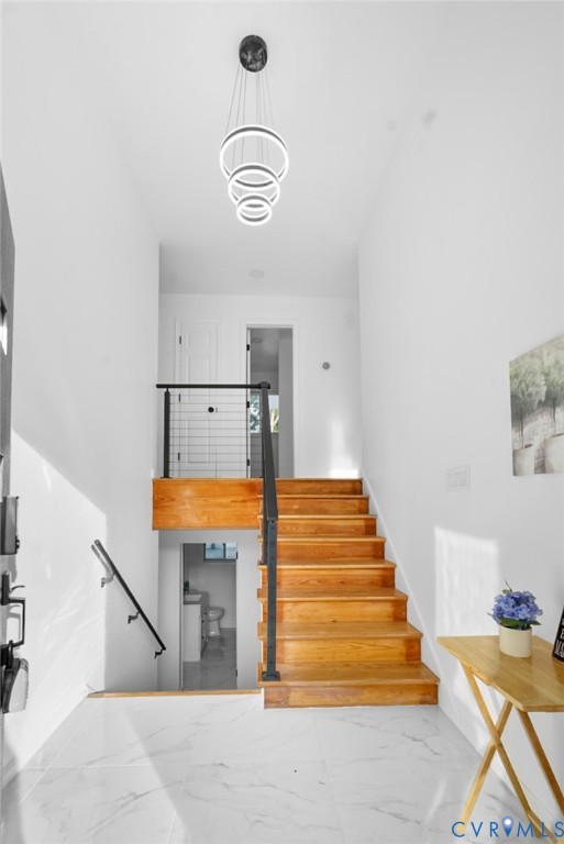 White marble-finish tile flooring, hardwood stairs, contemporary tiered chandelier, black metal stair railing, and white walls White marble-finish tile flooring, hardwood stairs, contemporary tiered chandelier, black metal stair railing, and white walls