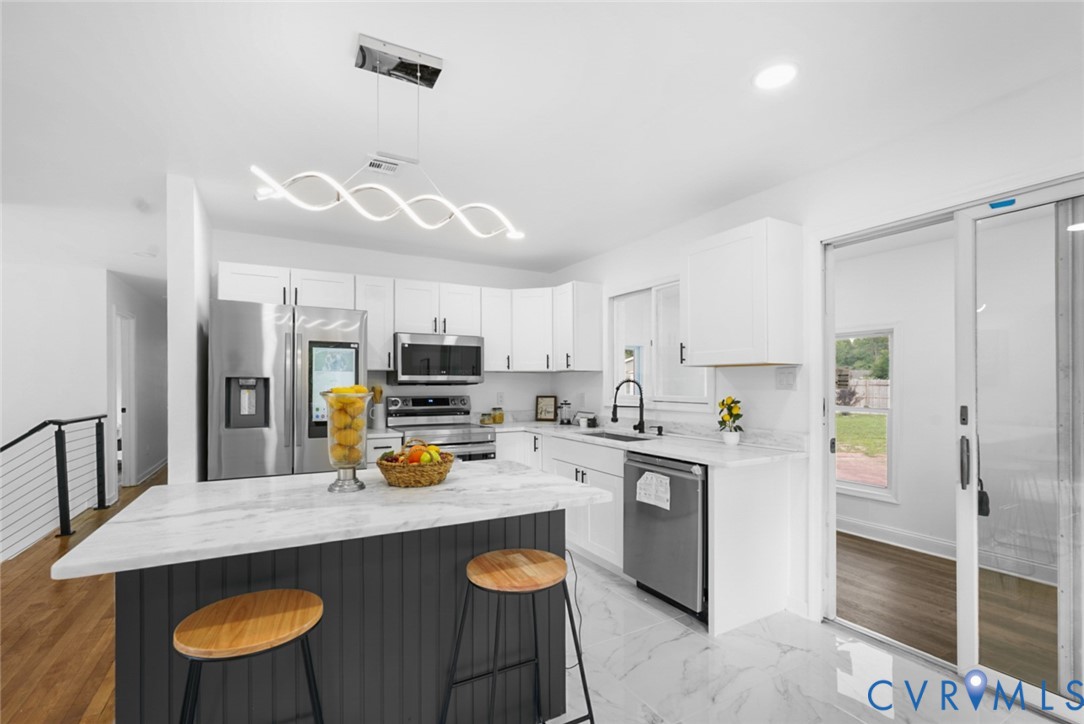 Kitchen featuring a center island with a stone countertop, white cabinetry with dark hardware, stainless steel appliances, and a modern linear chandelier