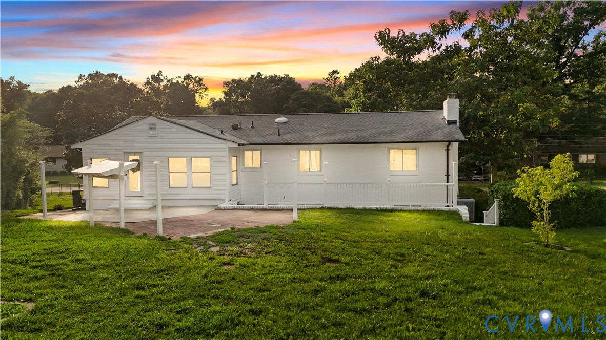 White siding exterior with dark shingle roofing, featuring a covered patio, a back deck with railing, and a chimney