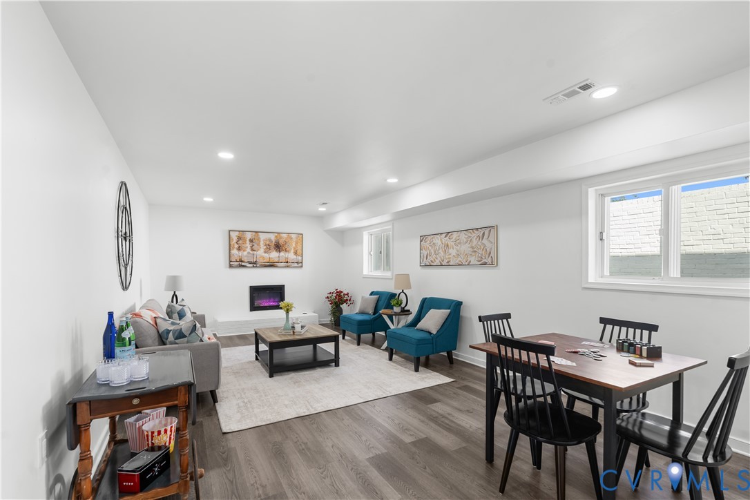 Recessed lighting illuminates the open-concept space, featuring wood-finish flooring and an electric fireplace