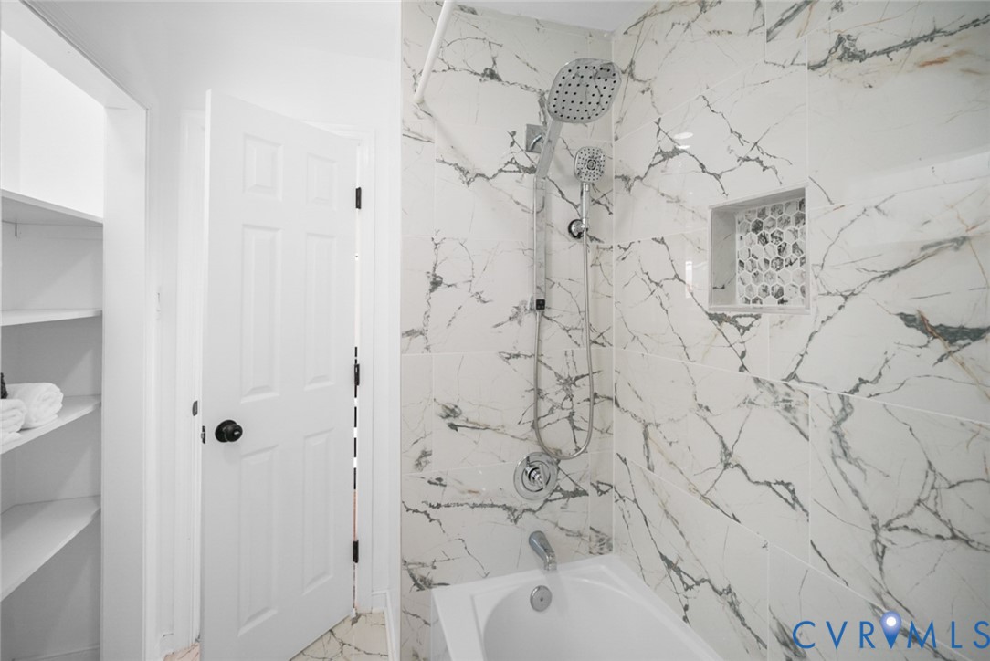 Bathtub with a chrome fixture, shower system featuring a handheld sprayer, built-in tiled niche, and marble-look wall tiling
