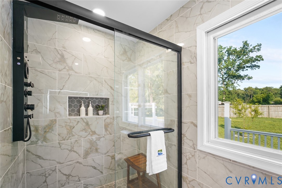 Walk-in shower with a black-framed glass enclosure, light-toned tiled walls, built-in tiled niche, and a window providing natural light