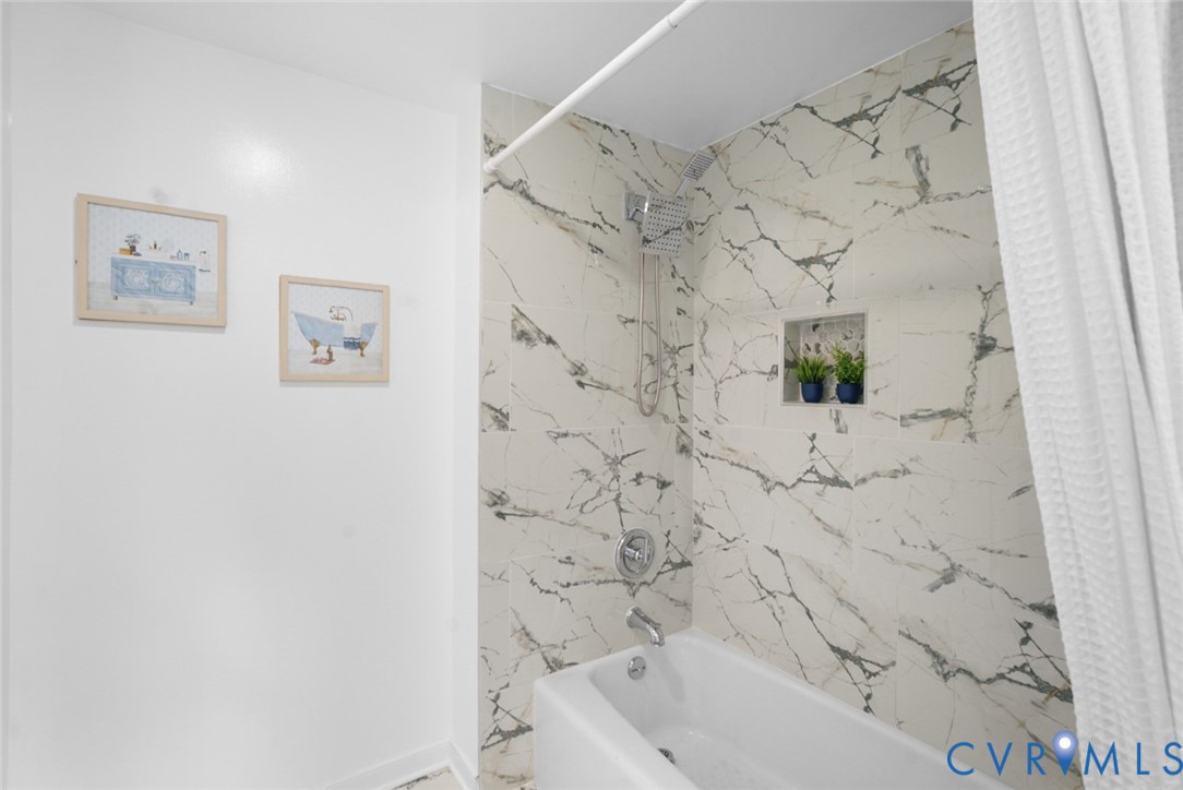 Bathtub with chrome fixtures, rainfall showerhead, and a tiled shower surround with an integrated niche