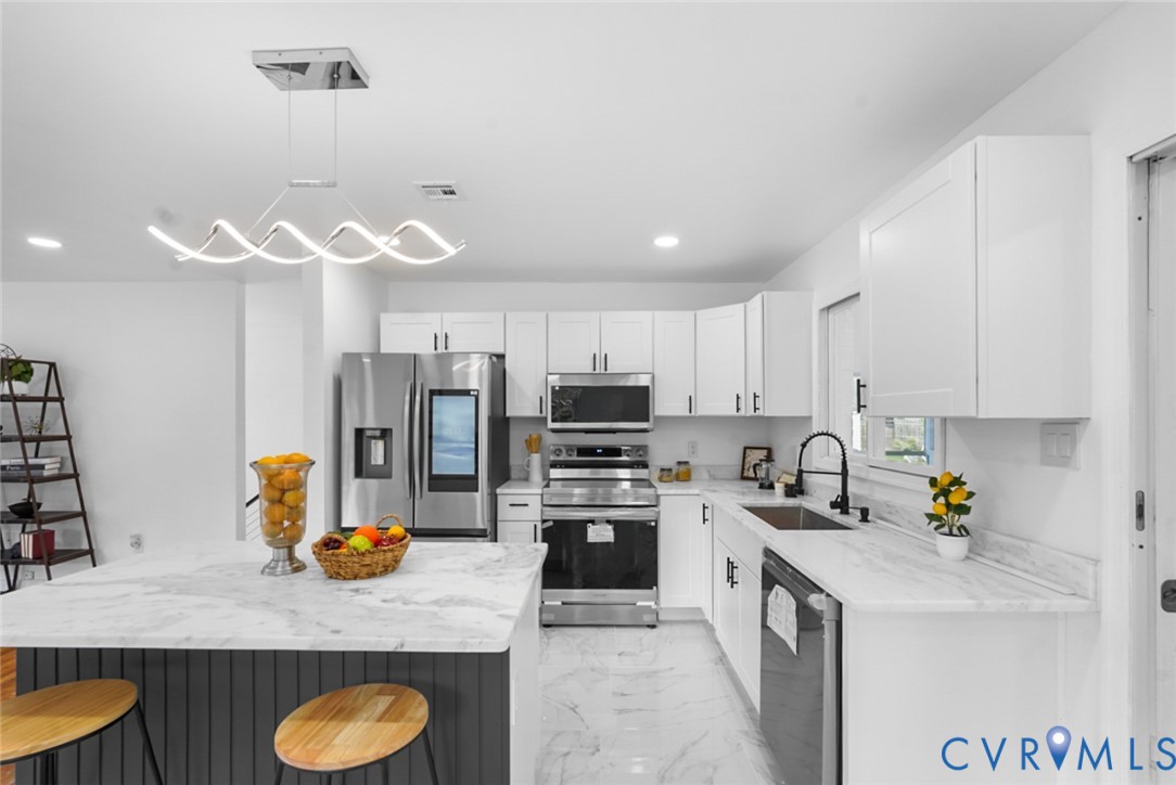 White cabinetry, stainless steel appliances, marbled countertops, and a contemporary linear chandelier