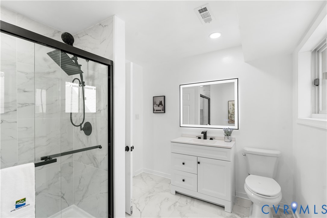 White vanity with black hardware, back-lit mirror, and white countertop