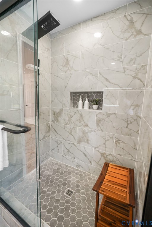 Walk-in shower with clear glass enclosure, large format tile walls, matte black shower head, and an integrated tiled niche