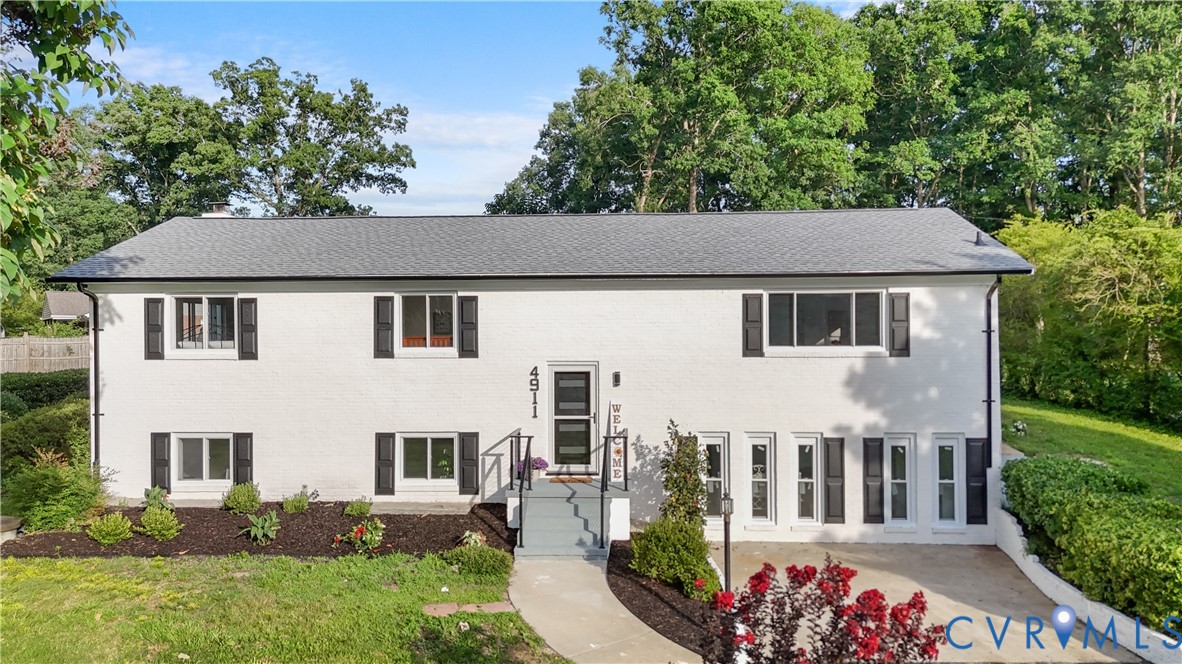 White brick exterior with a dark shingle roof, black shutters, and a well-maintained entry garden White brick exterior with a dark shingle roof, black shutters, and a well-maintained entry garden