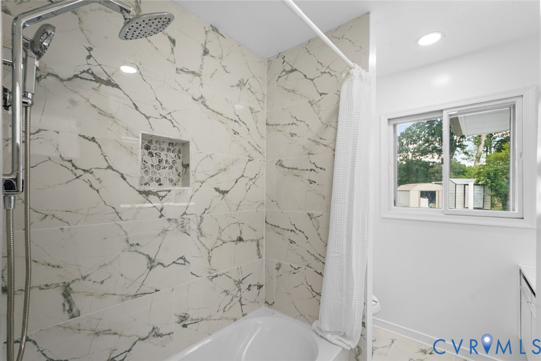Bathtub with a shower featuring a rain showerhead, a handheld shower, and a tiled niche