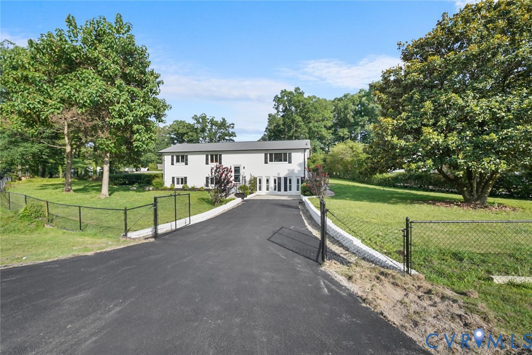 White exterior residence with dark shutters, a paved driveway, and mature landscaping White exterior residence with dark shutters, a paved driveway, and mature landscaping