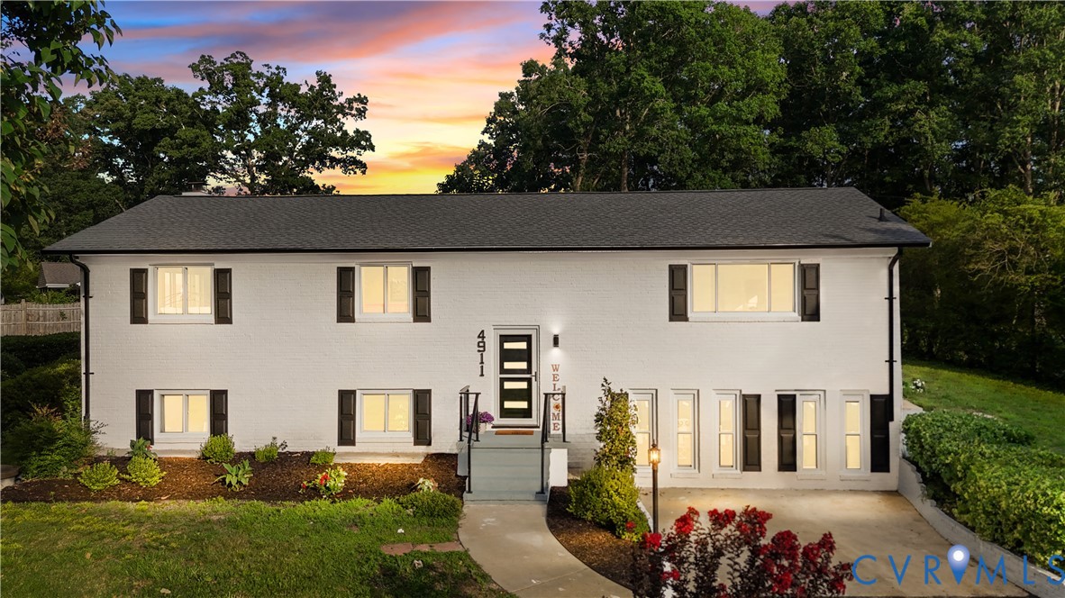 White exterior with dark shutters, dark roof, front entry stairs, and front landscaping