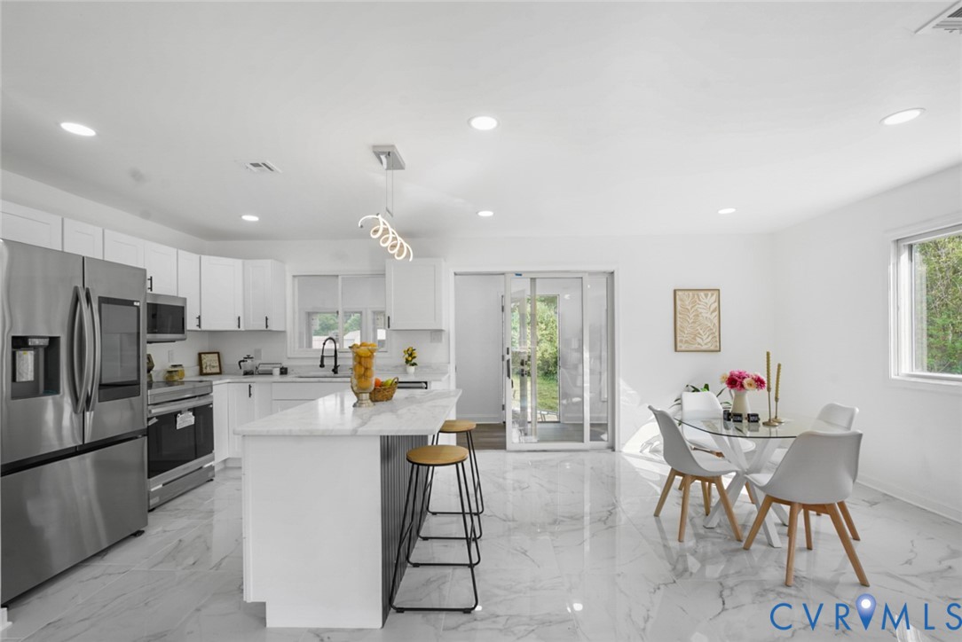 Open-concept kitchen and dining area featuring white cabinetry, stainless steel appliances, a center island with a stone countertop, and high-gloss tile flooring