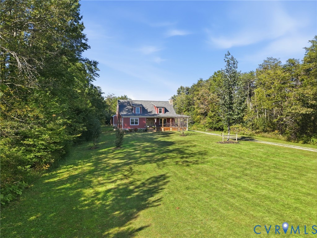 Two-story residence featuring a covered front porch, dormer windows, and a shingle roof, set on a sprawling grass lot surrounded by mature trees Two-story residence featuring a covered front porch, dormer windows, and a shingle roof, set on a sprawling grass lot surrounded by mature trees