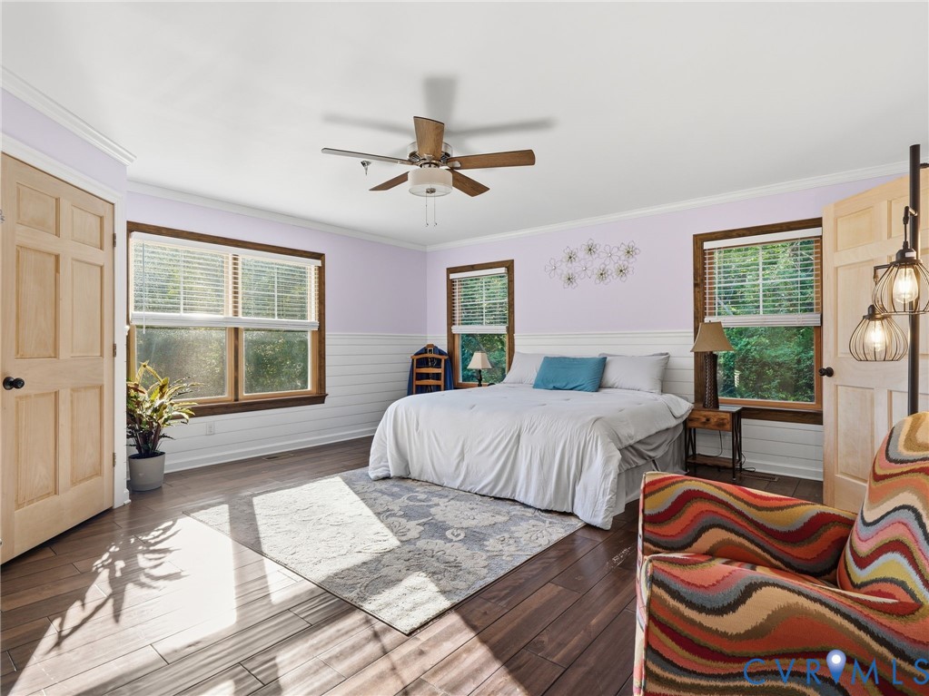 Room featuring dark wood-finish flooring, light-toned wood-finish panel doors, white wainscoting, multiple windows with dark wood trim, and a ceiling fan with integrated lighting