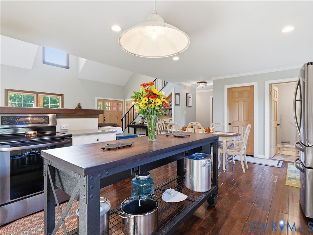 Kitchen featuring wood-finish flooring, a metal-framed kitchen island with a wood countertop, recessed lighting, a pendant light fixture, and stainless steel appliances