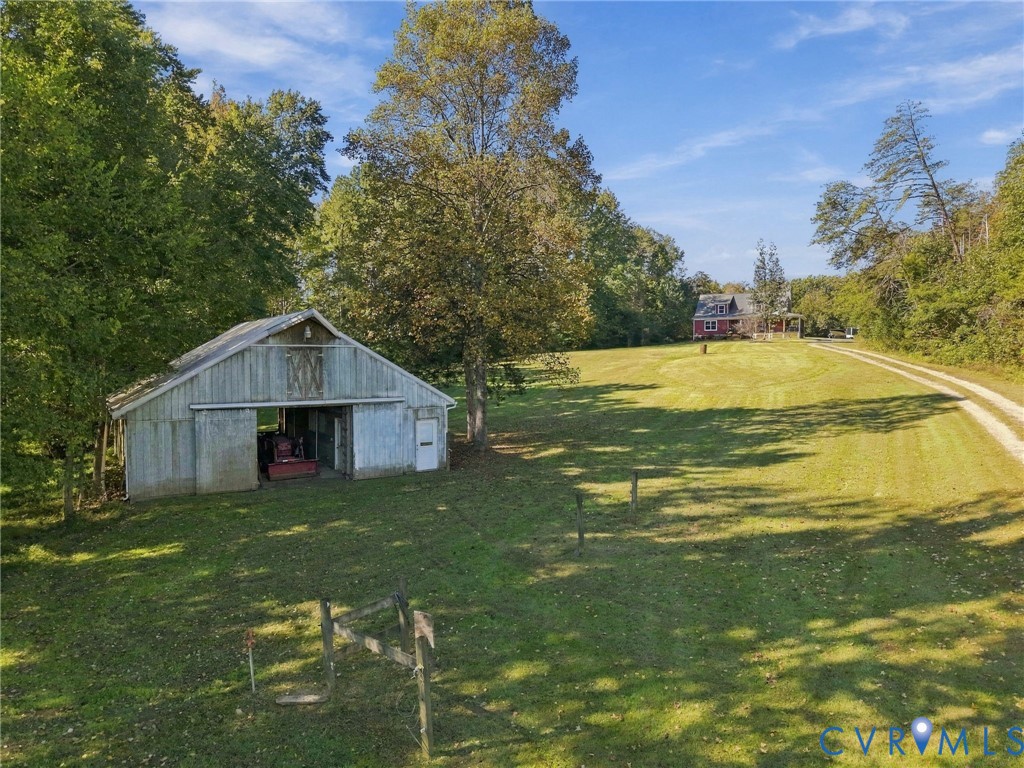 Expansive acreage featuring a wooden barn, gravel driveway, open lawn, and mature trees