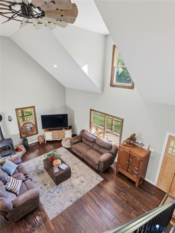 Vaulted ceiling with an industrial-style windmill ceiling fan, wood-finish flooring, wood-burning stove on a stone hearth, and multiple windows