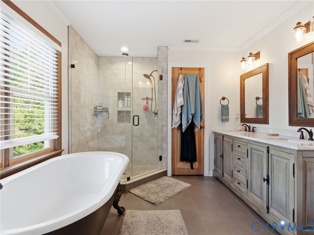 Freestanding soaking tub, glass-enclosed shower with tiled surround, double-sink vanity with stone countertop, and wood-framed vanity mirrors