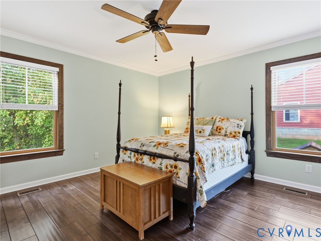 Wood-finish flooring, dual windows with dark-stained trim, and a ceiling fan with integrated lighting