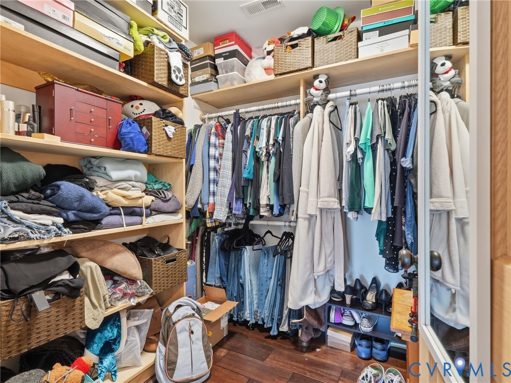 Walk-in closet featuring multi-tiered wood-finish shelving, overhead storage compartments, integrated hanging rods, and wood-finish flooring