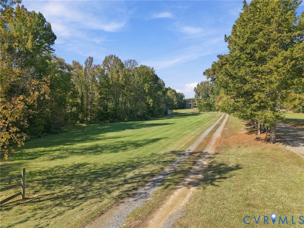 Expansive acreage featuring a manicured lawn, tree-lined perimeter, and a gravel drive