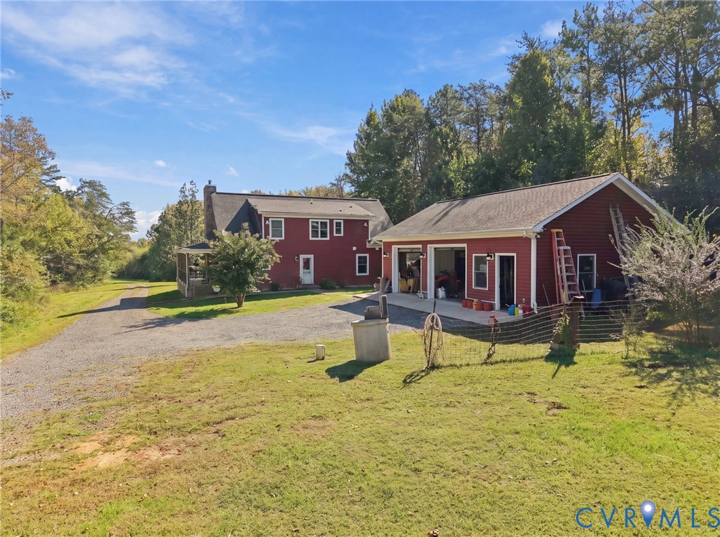 Two-story residence with red siding, detached multi-bay garage, stone-finish driveway, and expansive lawn area Two-story residence with red siding, detached multi-bay garage, stone-finish driveway, and expansive lawn area