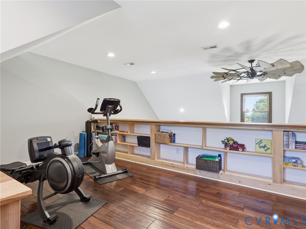 Finished room with wood-finish flooring, custom built-in low-profile shelving, recessed lighting, and an oversized decorative ceiling fan