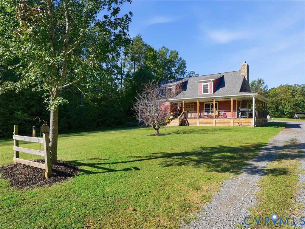 Two-story home with a wrap-around porch, stone chimney, wood-paneled exterior, asphalt shingle roof, and expansive front lawn Two-story home with a wrap-around porch, stone chimney, wood-paneled exterior, asphalt shingle roof, and expansive front lawn