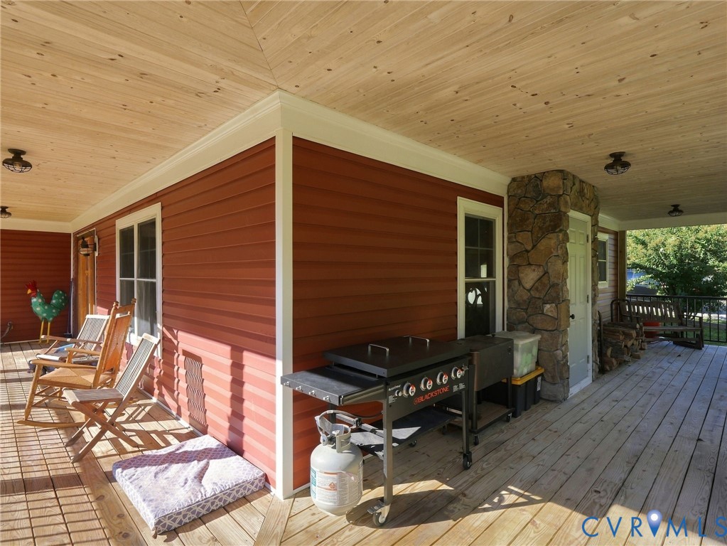 Wrap-around porch featuring wood-finish decking, natural wood-paneled ceiling, stone veneer pillar, and exterior lighting fixtures Wrap-around porch featuring wood-finish decking, natural wood-paneled ceiling, stone veneer pillar, and exterior lighting fixtures