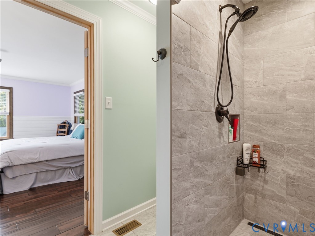 Walk-in shower featuring large-format grey stone-finish tile, oil-rubbed bronze shower fixtures, and a recessed wall niche