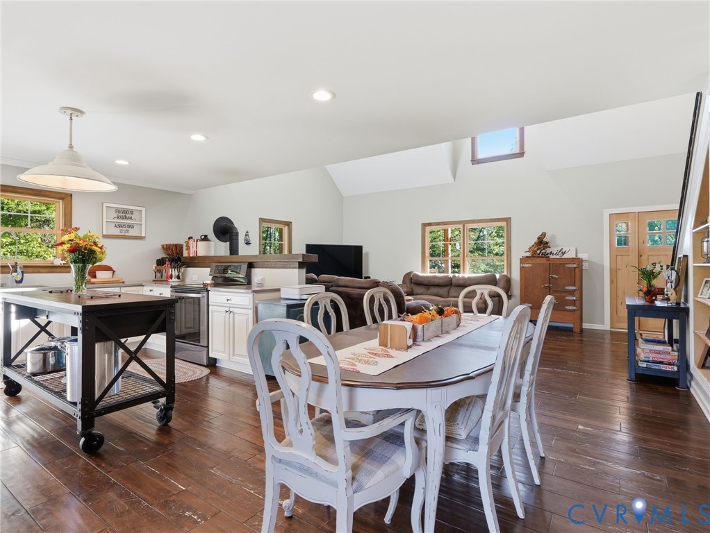 Open concept kitchen and dining area featuring wood-finish flooring, vaulted ceilings, recessed lighting, a kitchen island with industrial casters, and wood-framed windows