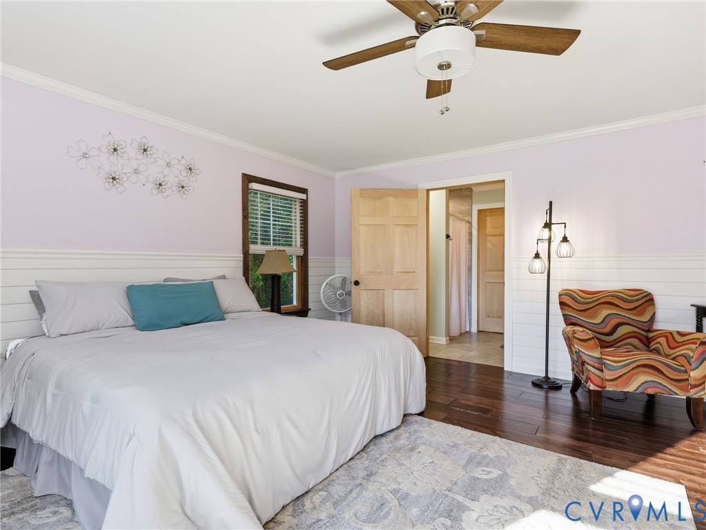 Room featuring dark-stained wood-finish flooring, horizontal shiplap wall paneling, crown molding, and a central ceiling fan with integrated lighting
