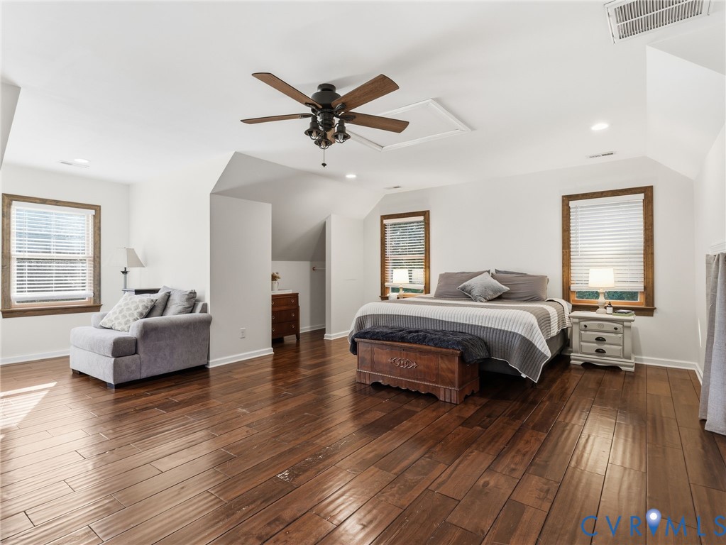 Spacious room featuring wood-finish flooring, vaulted ceilings, a central ceiling fan with integrated lighting, and multiple windows framed by wood trim