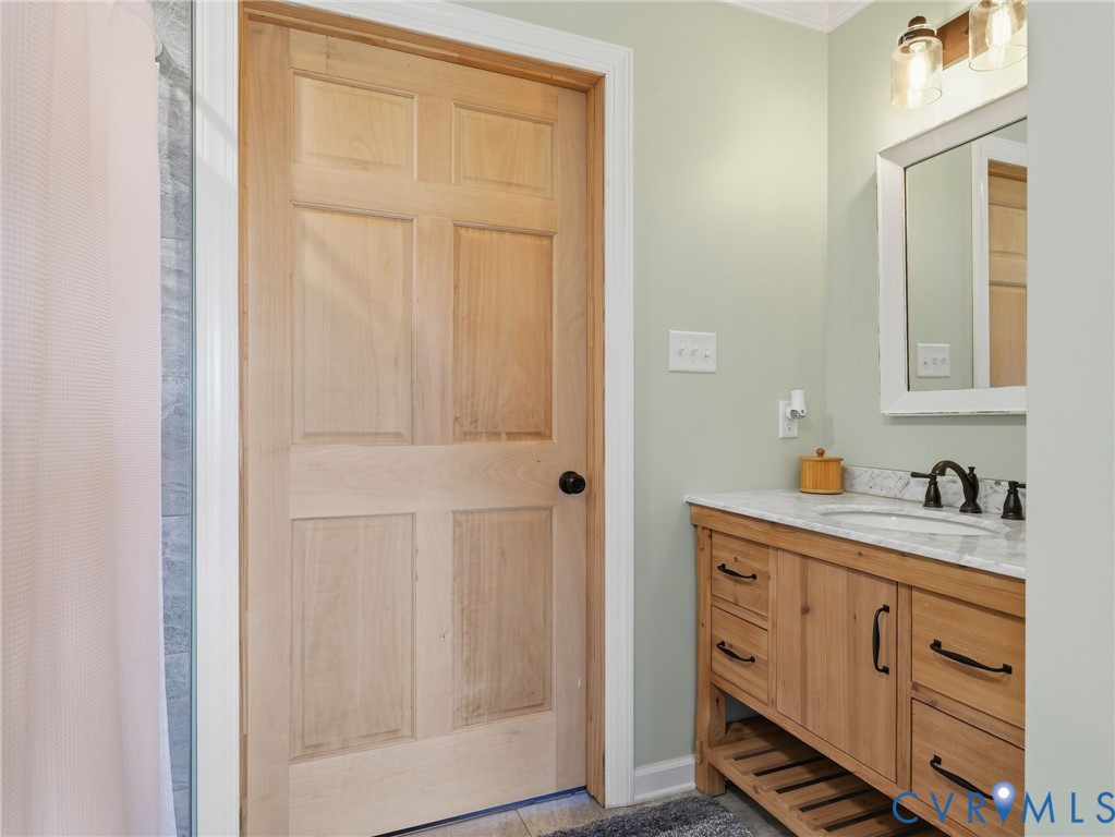 Bathroom featuring a natural wood-finish vanity with stone-top surfacing, undermount sink, matte black hardware, and matching solid wood six-panel door