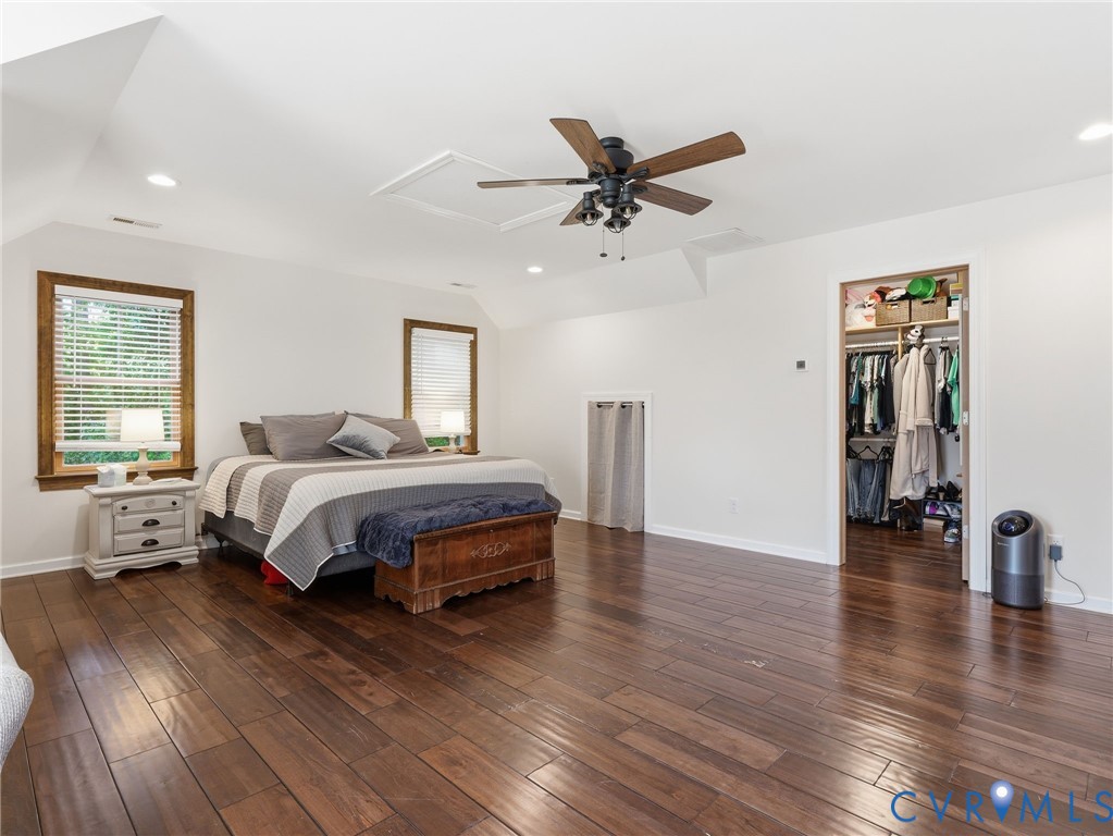 Spacious room featuring wood-finish flooring, vaulted ceilings, recessed lighting, a ceiling fan, and built-in wall storage access