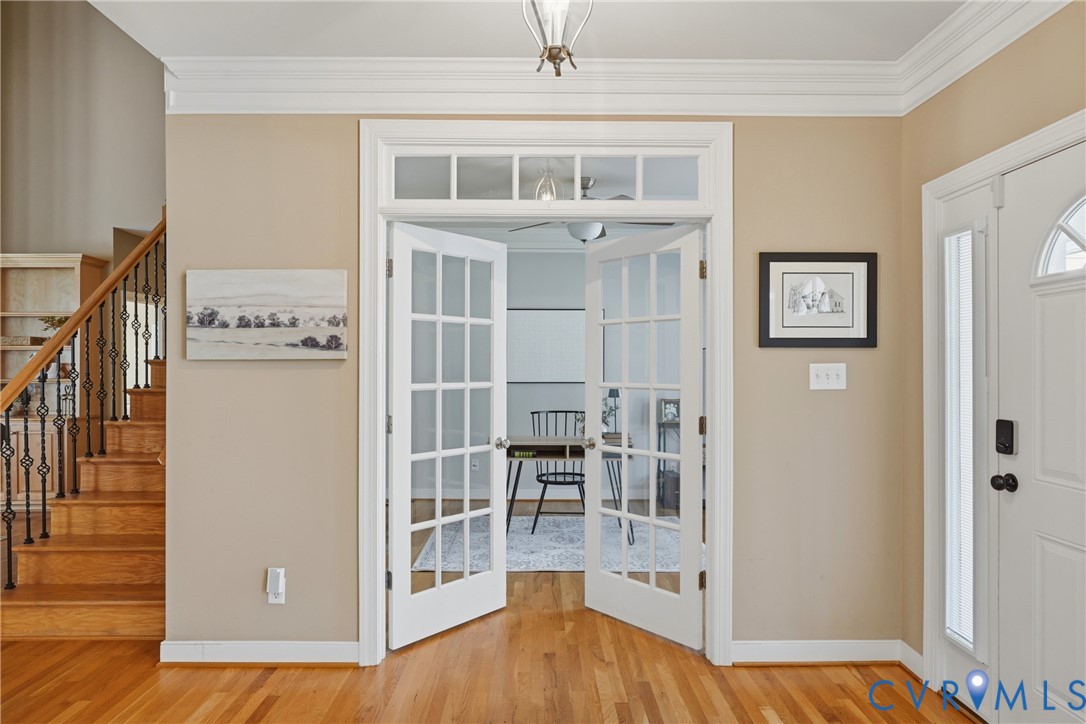 Interior entryway featuring wood-finish flooring, double glass-paneled French doors with a transom window, and a staircase with an ornamental metal balustrade