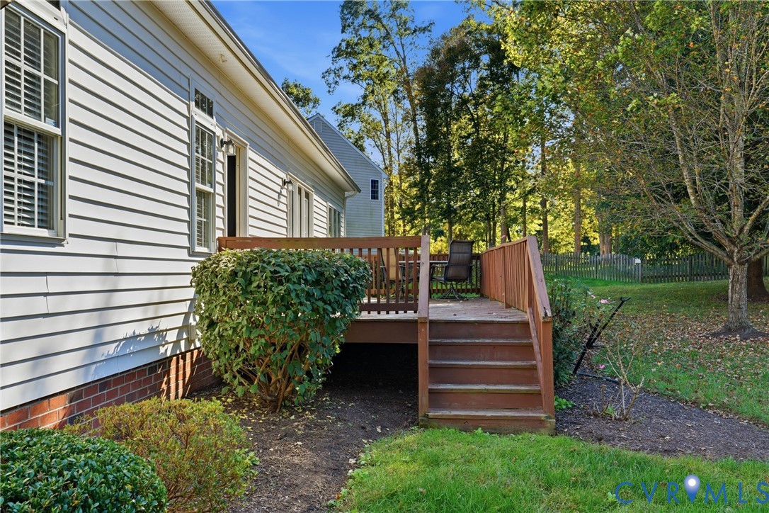 Rear exterior featuring horizontal lap siding, brick foundation, raised wood deck with integrated stairs, and landscaped yard