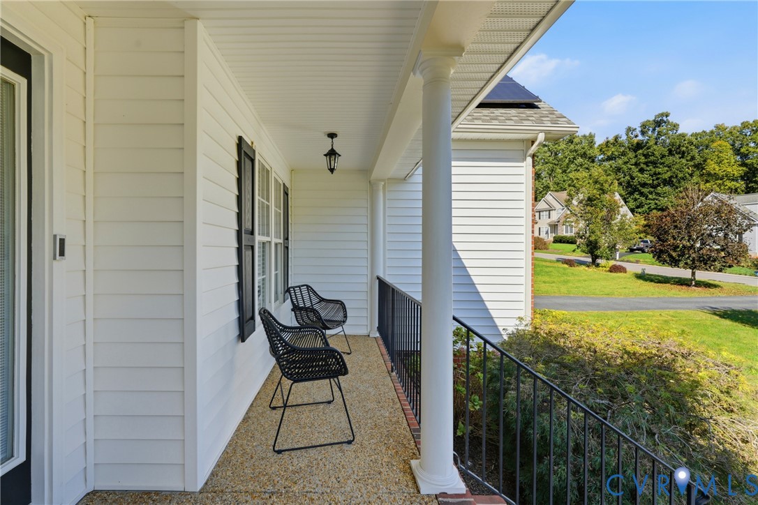 Covered front porch featuring white horizontal siding, round support columns, a textured aggregate floor, and black metal railings