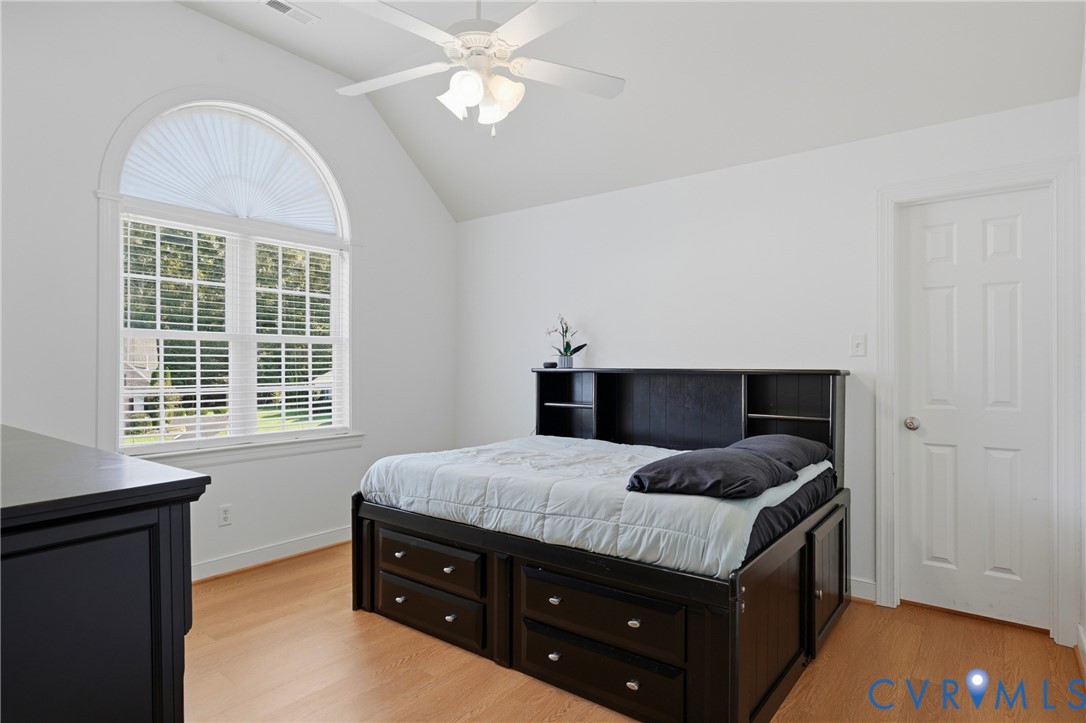 Vaulted ceiling featuring a central ceiling fan with integrated lighting, a large arched window with muntin detailing, and light-toned wood-finish flooring