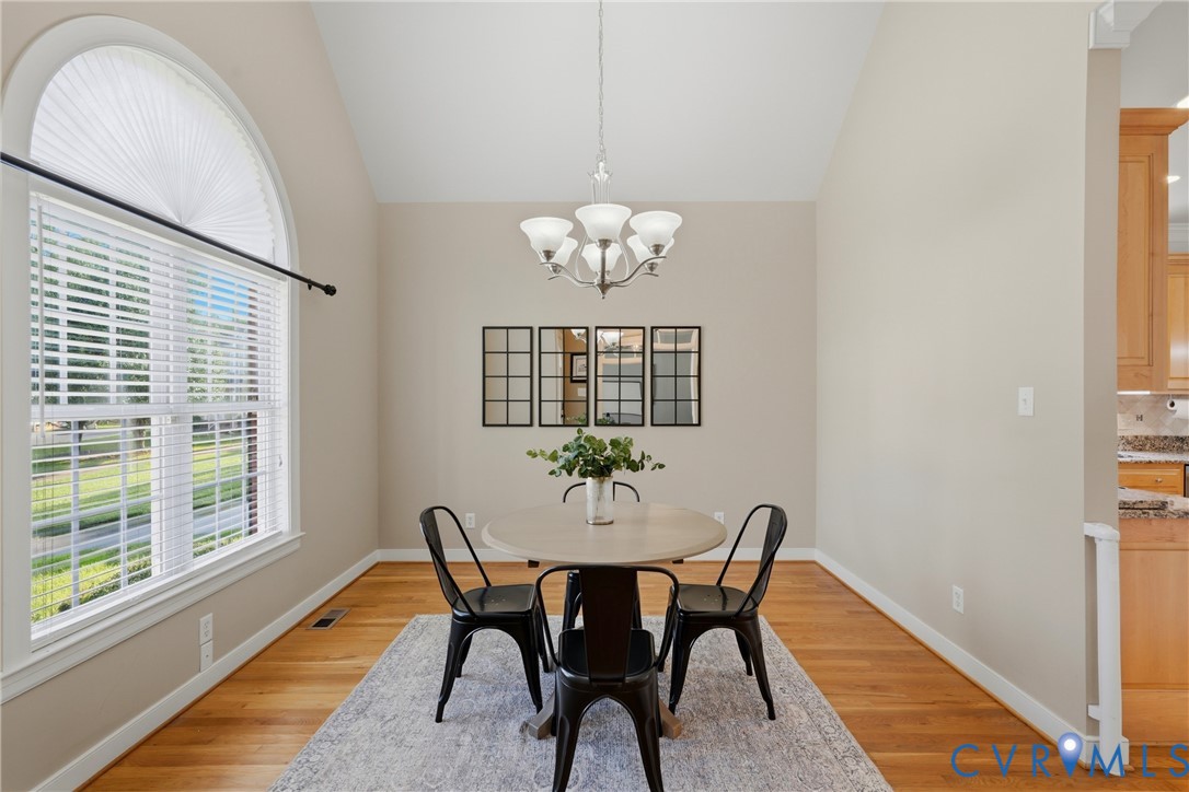 Vaulted ceilings, expansive arched window with grid detailing, wood-finish flooring, and a multi-light chandelier