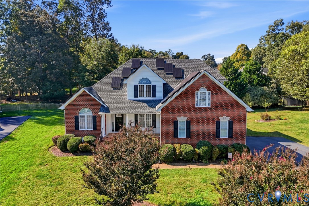 Traditional brick exterior featuring a multi-gabled roofline, solar panel installation, arched window accents, and an expansive lawn