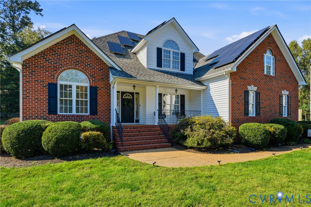 Multi-gabled brick and siding exterior featuring solar panel arrays, arched windows with shutters, and a front entry with brick steps and metal railings