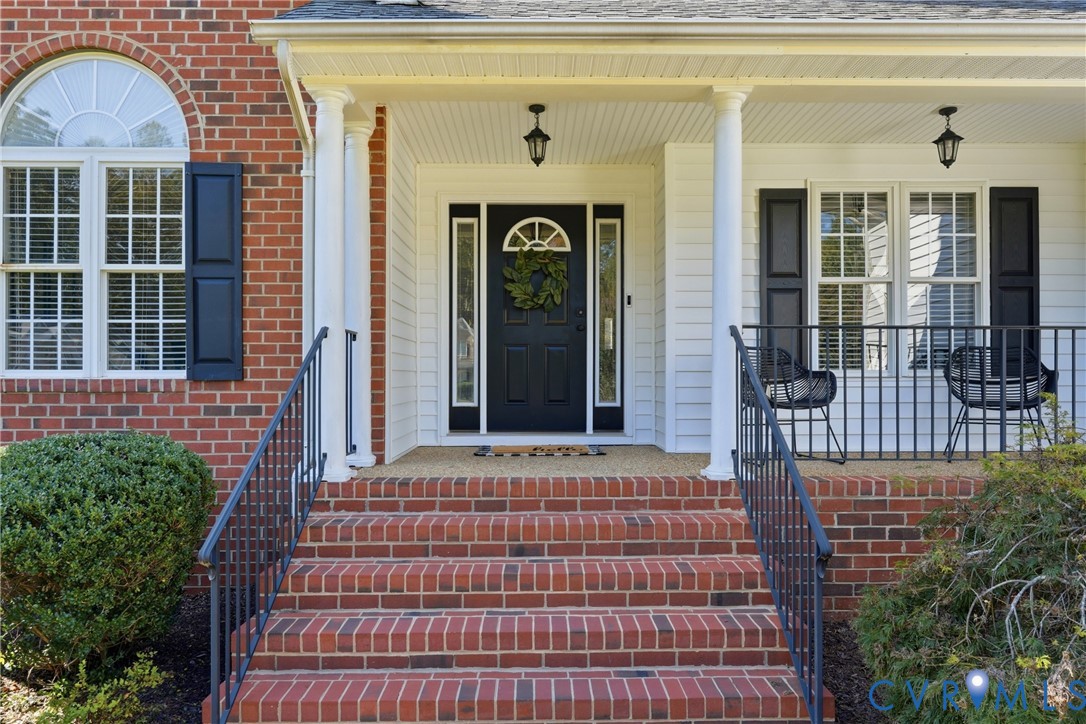 Covered front porch featuring red brick steps, white support columns, black metal railings, and a front entry door with a decorative transom window