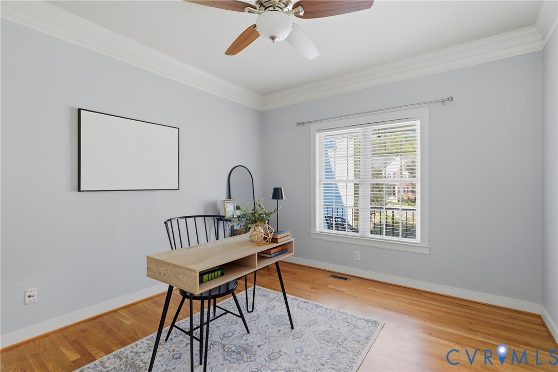 Wood-finish flooring, crown molding, and a multi-blade ceiling fan with a central light fixture