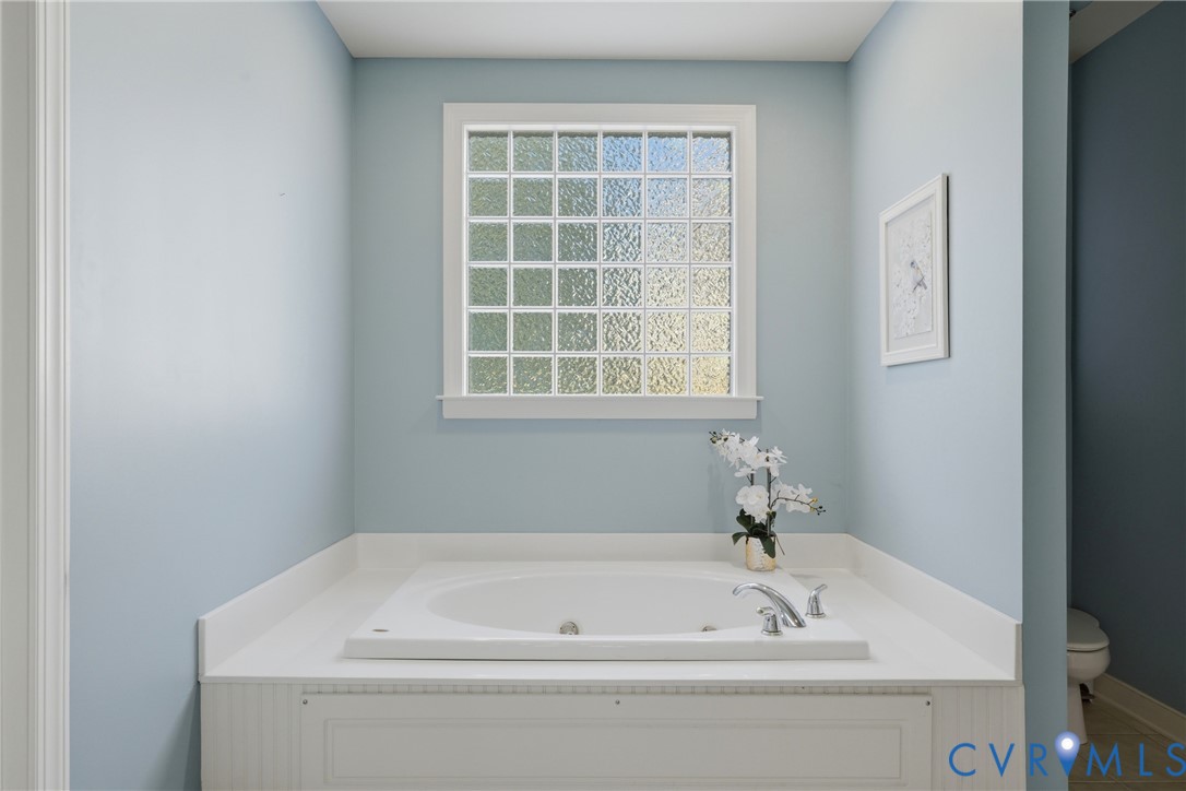 Built-in soaking tub with a white surround, featuring a grid-pattern glass block window and chrome-finish hardware