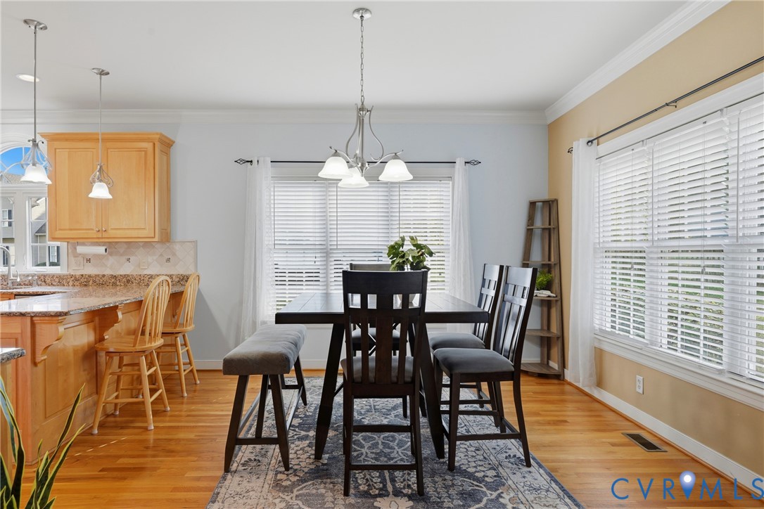 Hardwood flooring, kitchen island with stone-surface countertop, multi-light hanging chandelier, and crown molding