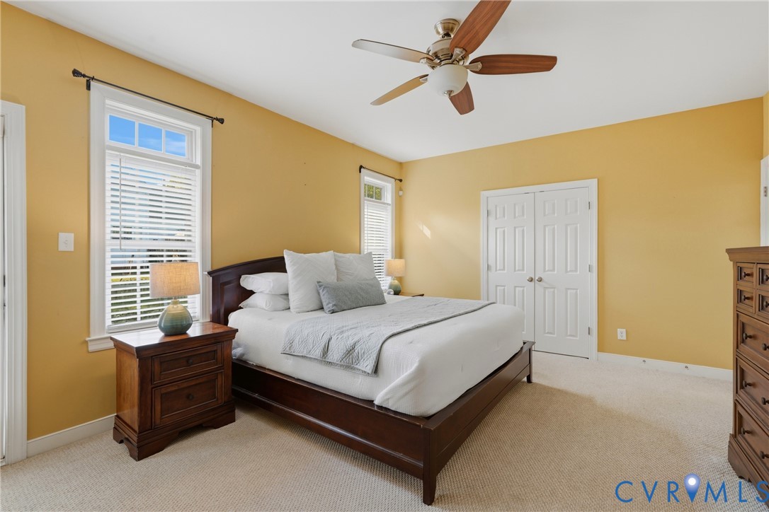 Room featuring neutral carpeting, dual double-hung windows, a ceiling-mounted fan with integrated light, and a double-door closet