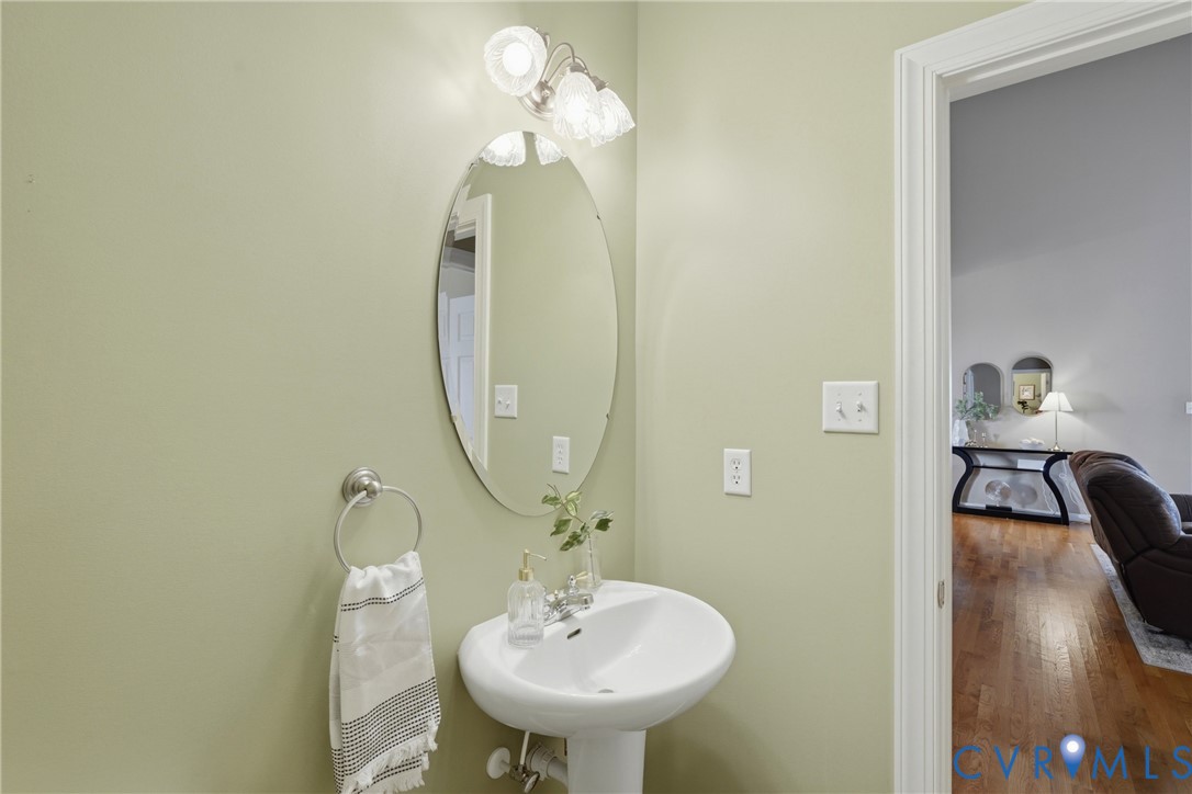 Pedestal sink with polished metal faucet, oval wall-mounted mirror, and multi-bulb decorative light fixture