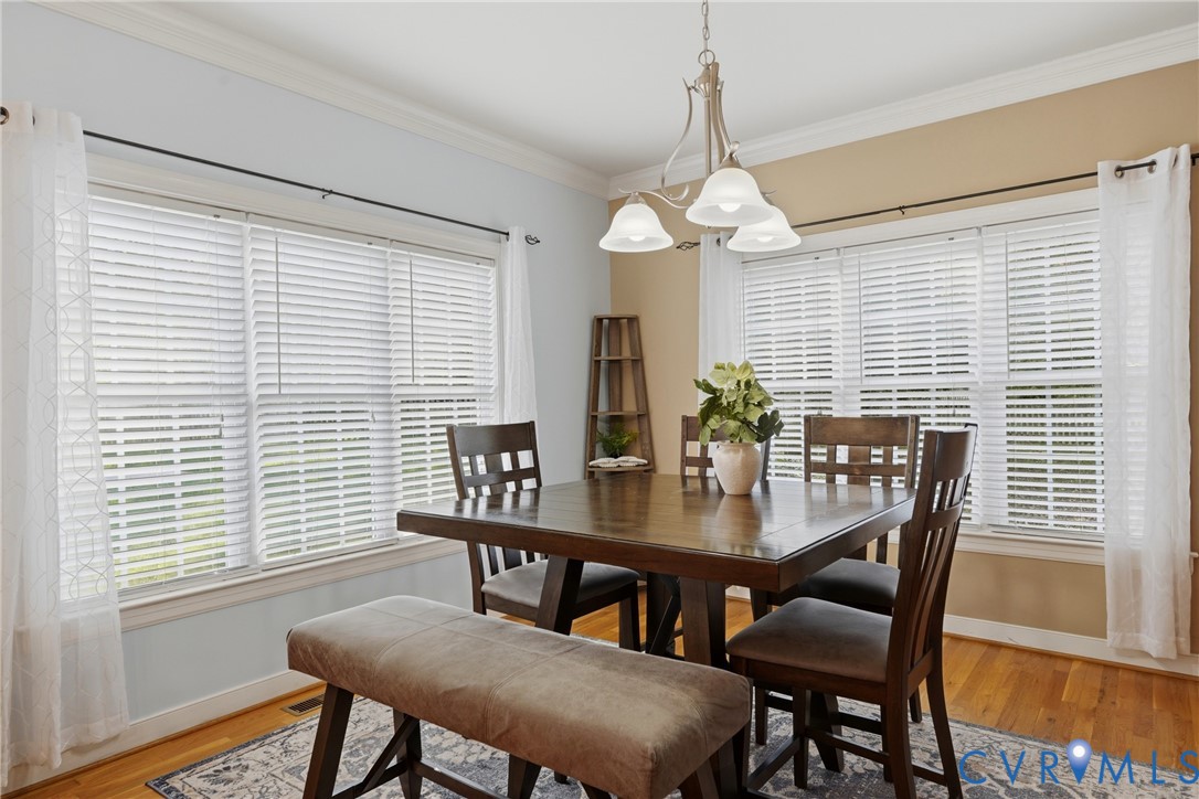 Multi-window dining area featuring crown molding, hardwood flooring, and a three-light chandelier