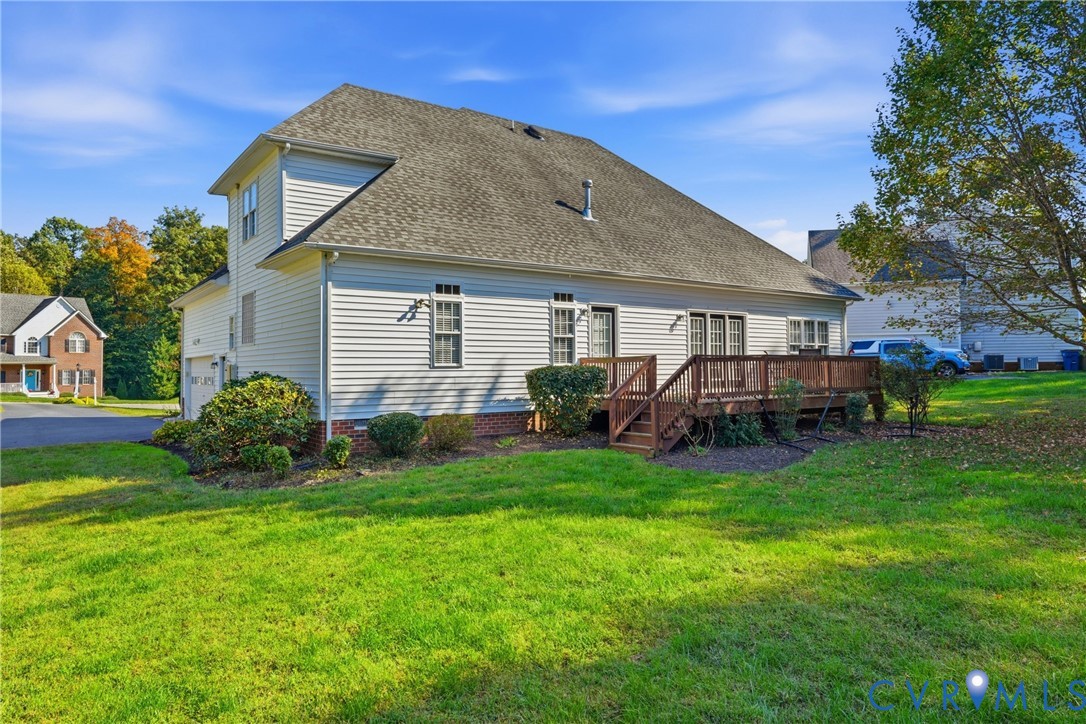 Exterior siding featuring a brick foundation, a raised wood deck with balustrades, an attached two-car garage, and a sodded yard