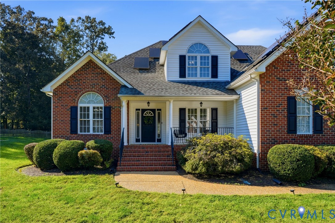 Multi-gabled brick and vinyl siding exterior featuring arched windows, a covered front porch with iron railing, brick entry steps, and roof-integrated solar panels
